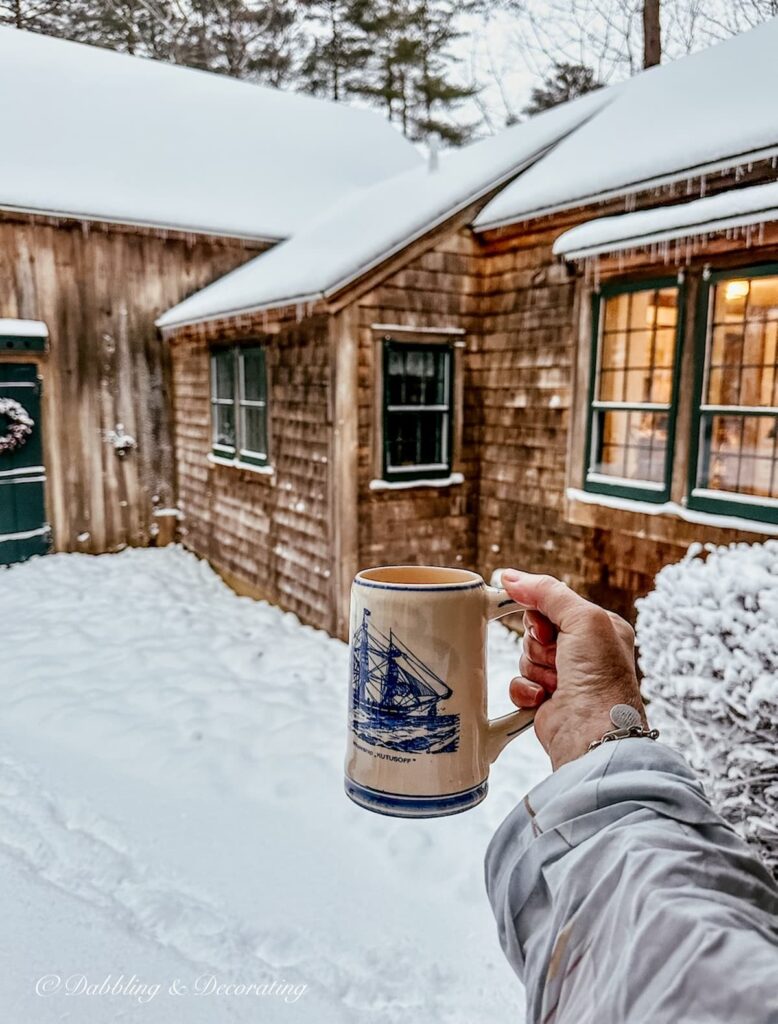 Blue and tan Delft mug in hand with coffee toasting to a snow day outside of cedar shakes home.