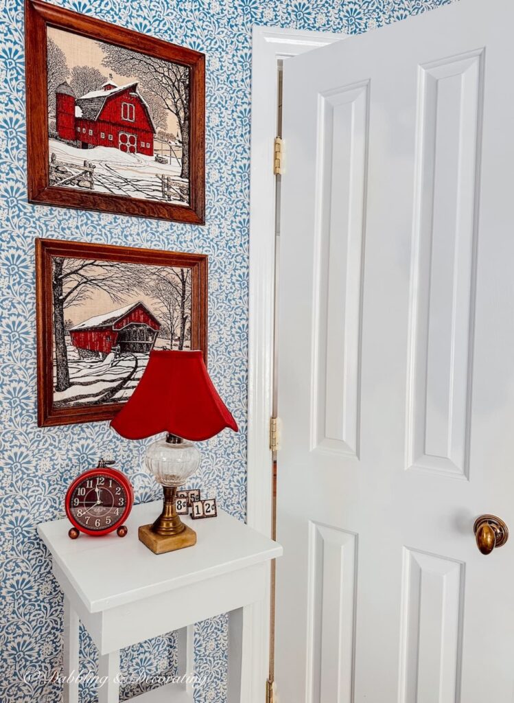 Two Kay Dee Linen Red winter scenery prints in wooden frames on  wall in bedroom with red lamp and blue bedroom wallpaper ideas.