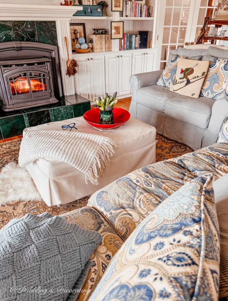 Cozy cottage style living room with white ottoman, pellet stove and red bowl styled with spring flowers from Goodwill home decor.