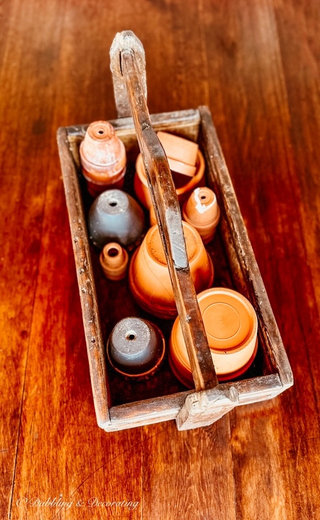 Toolbox filled with terracotta pots on wooden table outdoors.