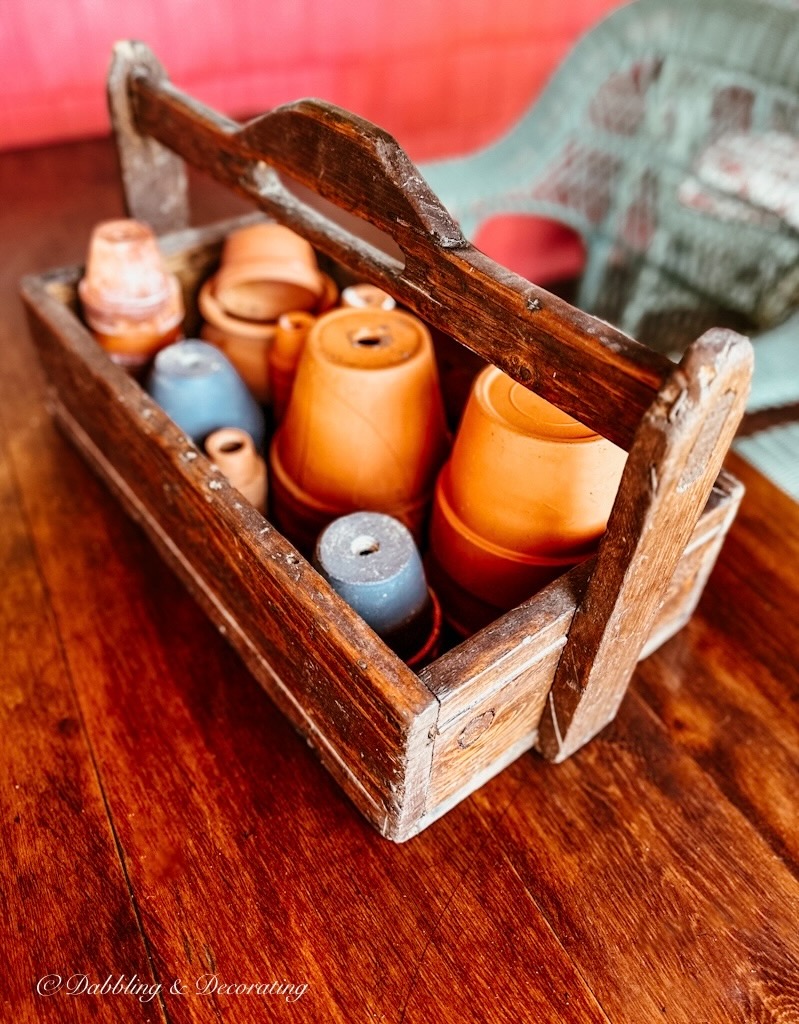 Toolbox filled with terracotta pots on wooden table outdoors.