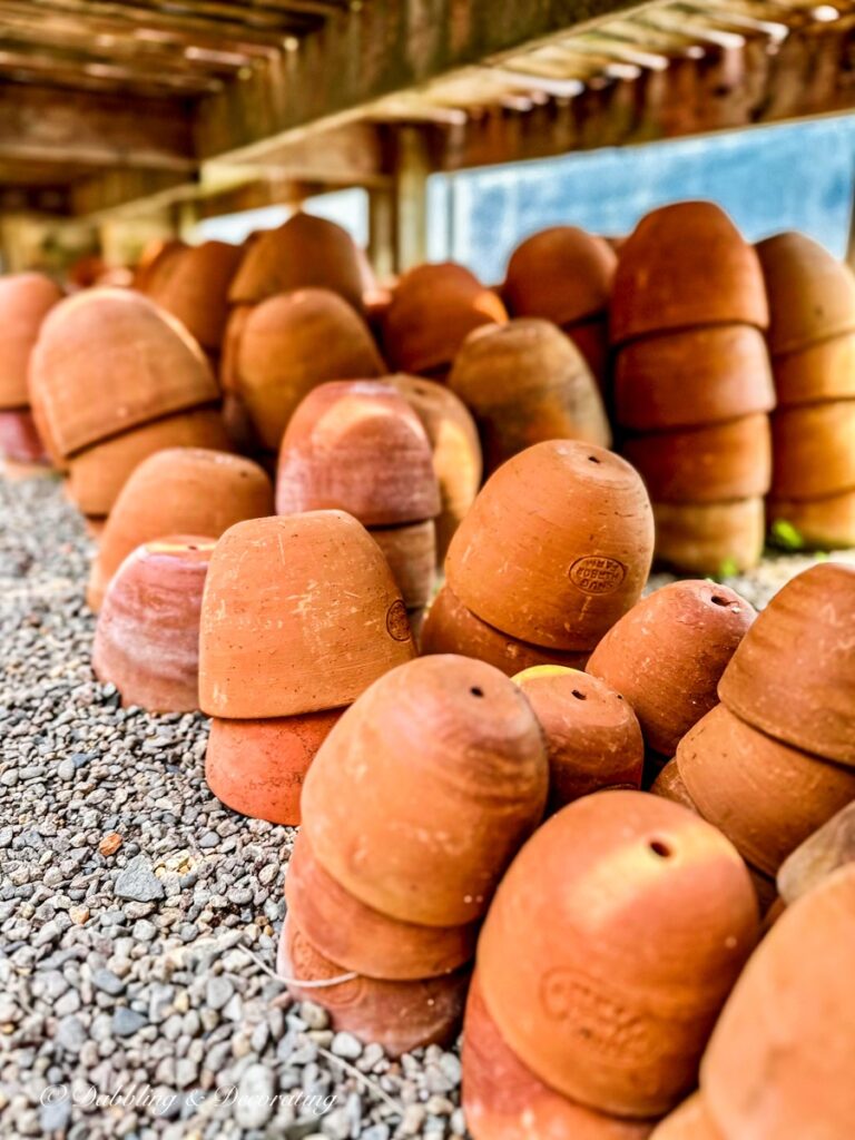 Large oval terracotta pots stacked in a barn on stones.